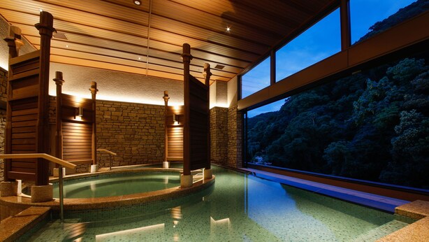 A spa area with a hot tub, wooden beams, stone walls, and a view of a forested hillside.