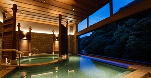 A spa area with a hot tub, wooden beams, stone walls, and a view of a forested hillside. - Yumekaiyu Awajishima (Sumoto)