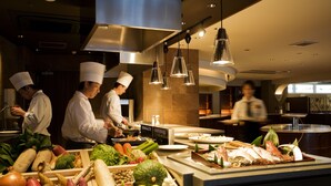 A modern kitchen with chefs preparing food, a buffet with various dishes, and a clean, well-lit environment.