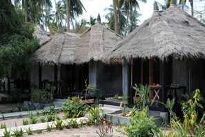 A tropical resort with thatched-roof huts, a garden with various plants, and palm trees in the background. - Secret Garden Village (Koh Tao)