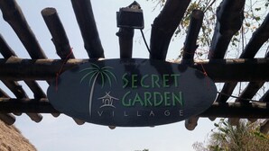 Ein Schild für 'Secret Garden Village' mit Palmenbäume-Logo und traditioneller Hüttenarchitektur.