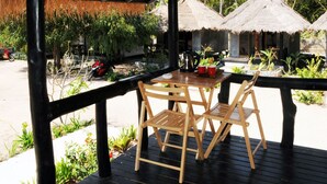 Eine Holzterrasse mit Tisch und Stühlen, umgeben von strohgedeckten Gebäuden und üppigem Grün.