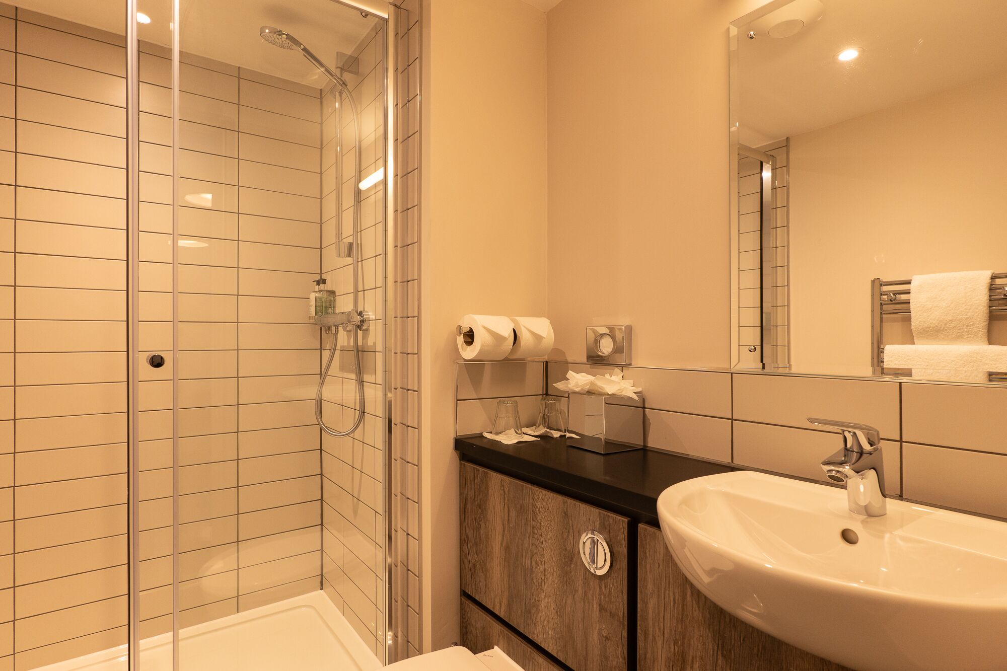 Un baño moderno con cabina de ducha de vidrio, un lavabo con espejo y un perchero para toallas.