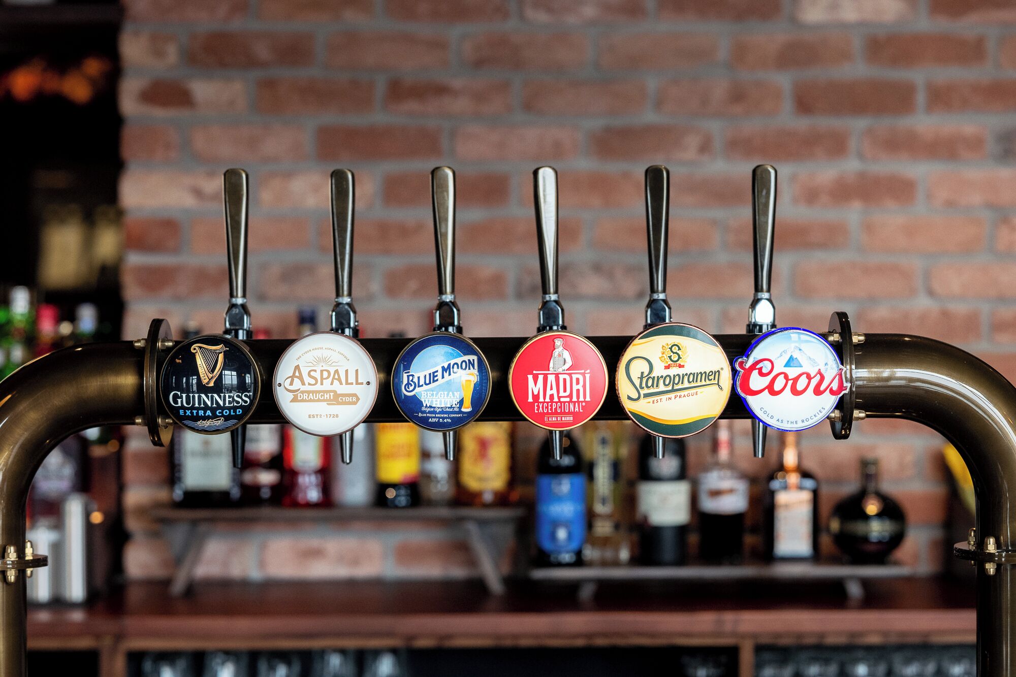 Un bar con pared de ladrillo y una fila de grifos de cerveza etiquetados con varias marcas.