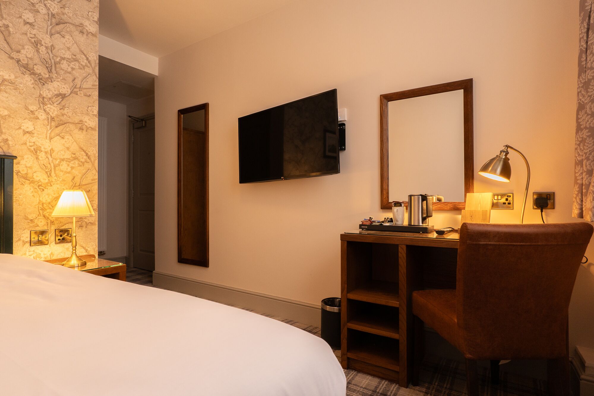 Una habitación de hotel con cama, escritorio con lámpara, televisor y espejo.
