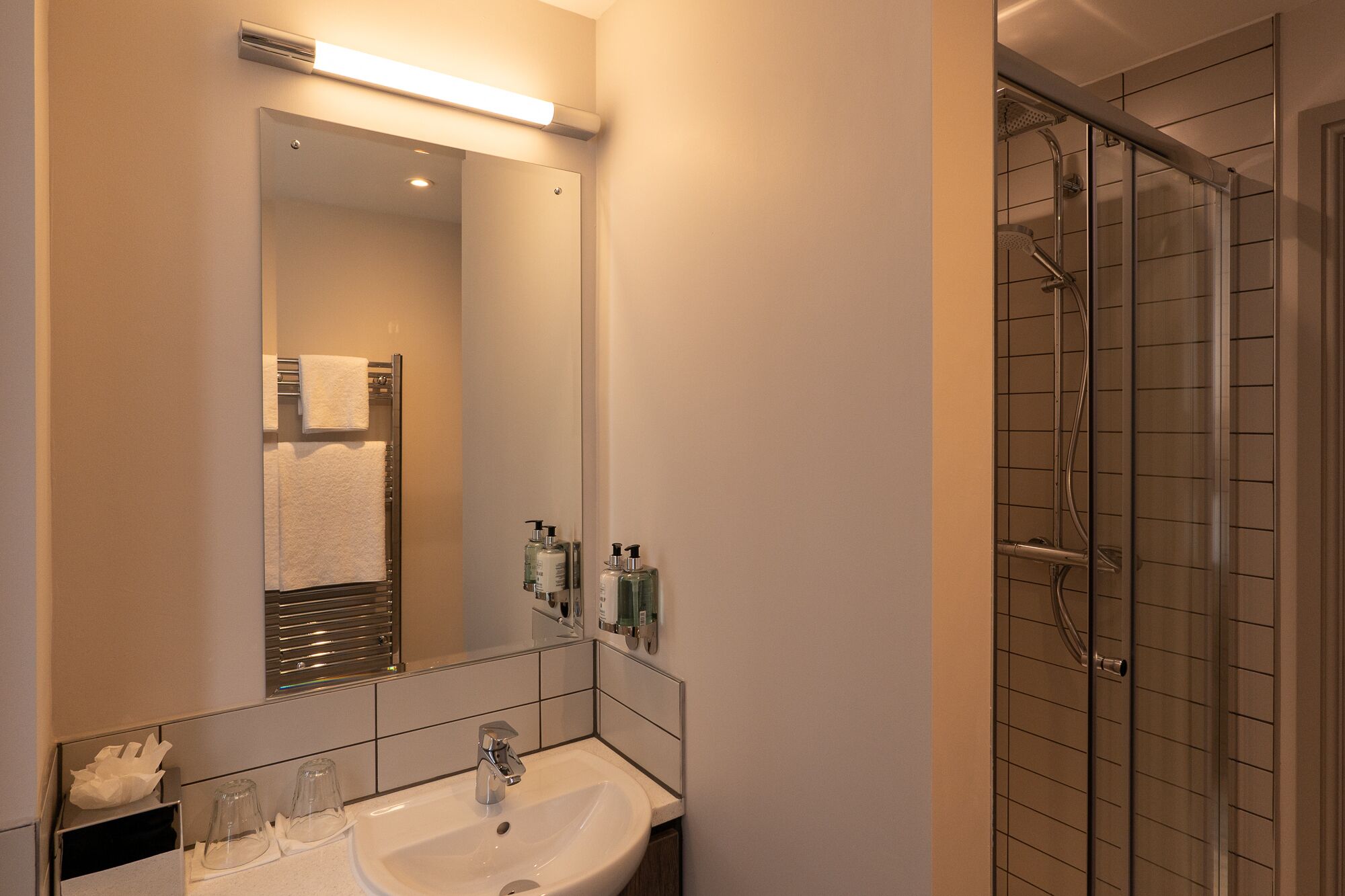 A bathroom with a large mirror, a sink, and a shower area.