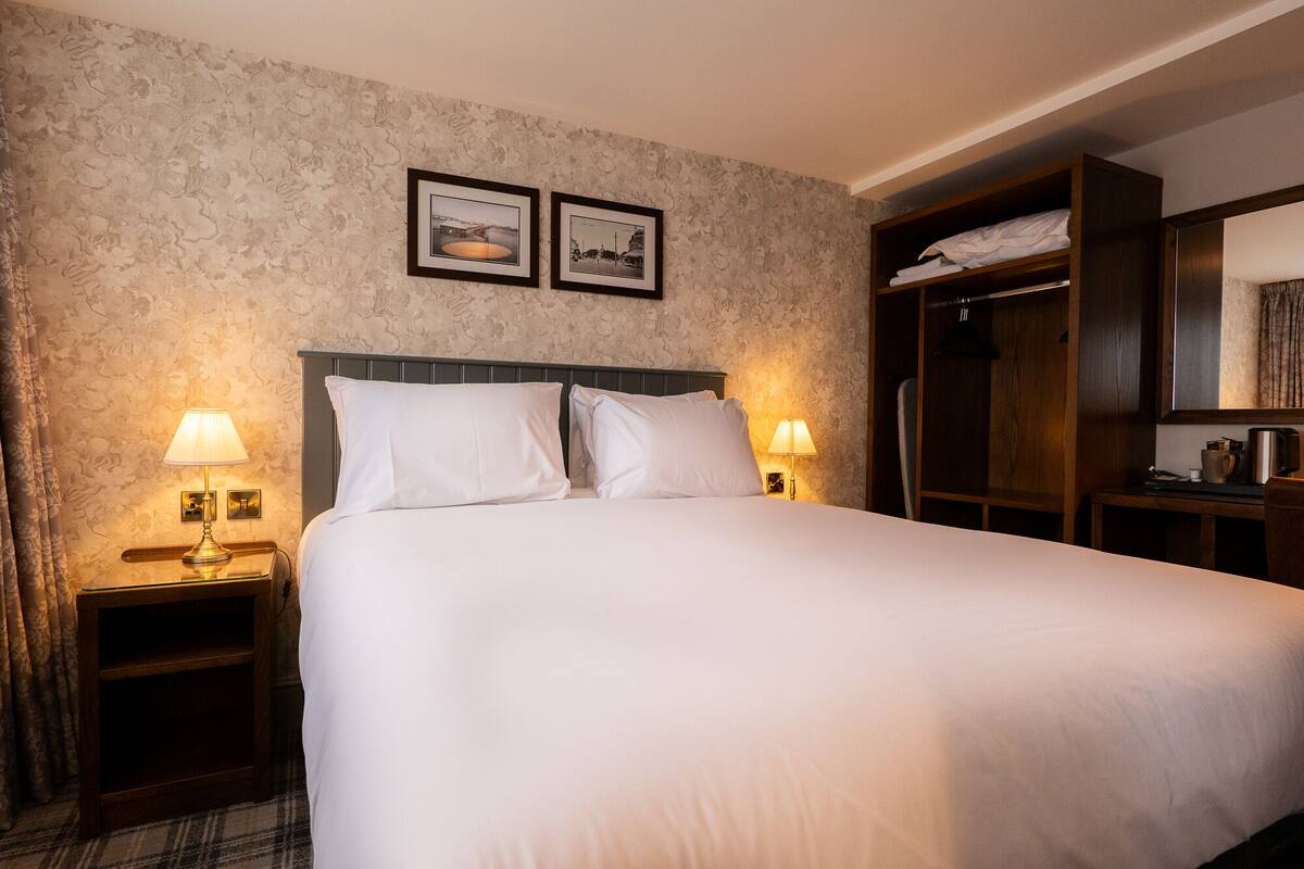 A neatly made bed with white linens, two bedside lamps, and a headboard. There are two framed pictures on the wall above the bed.