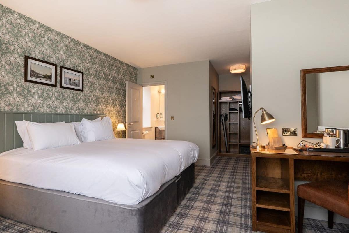 A hotel room with a bed, a desk with a lamp, a mirror, and a wardrobe.