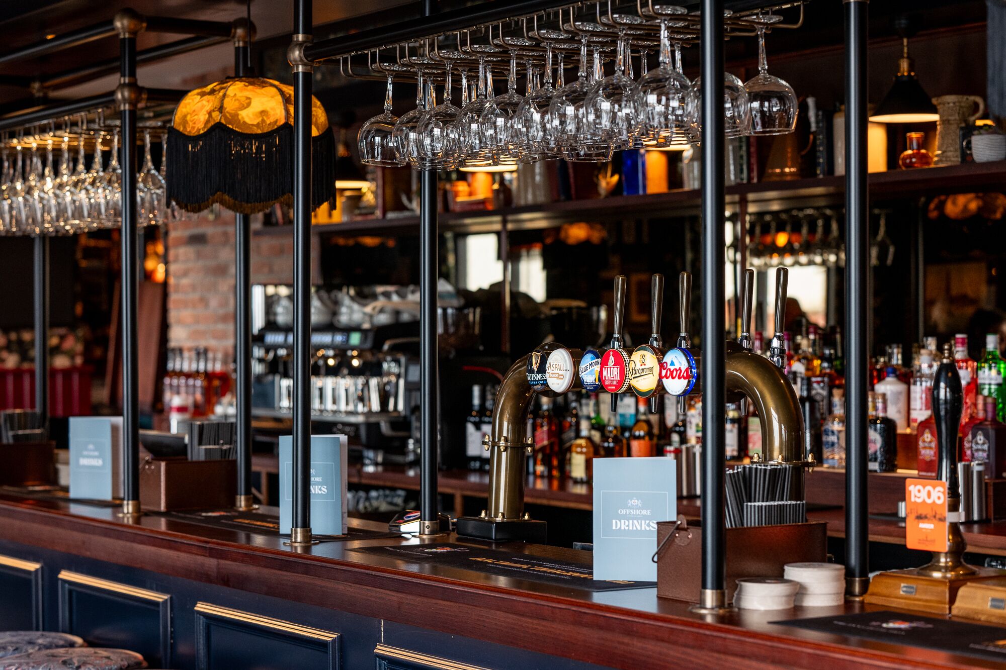 A bar area with multiple taps, glasses, and bottles.