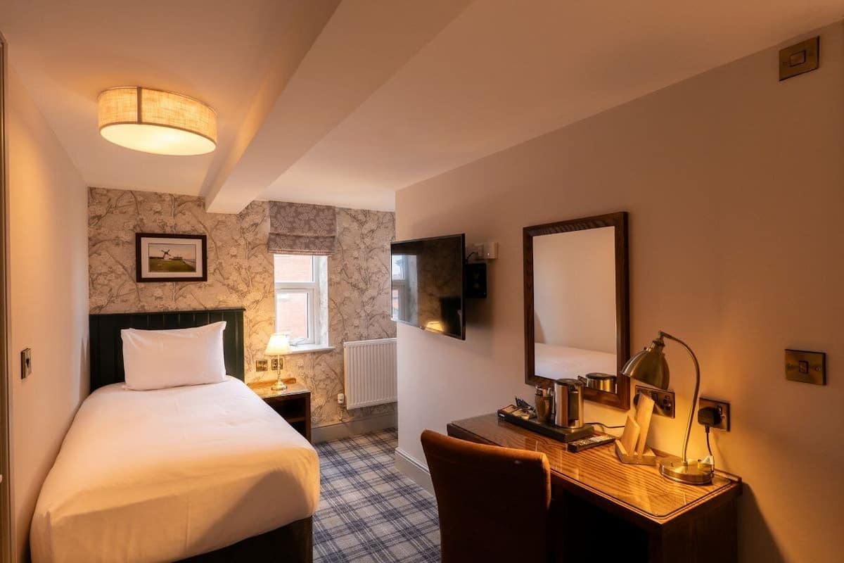 A hotel room with a bed, a desk, a chair, a lamp, a television, and a window.
