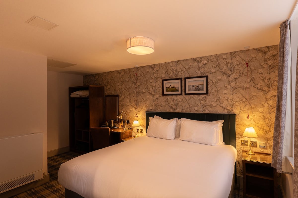 A hotel room with a large bed, two bedside lamps, a wardrobe, and a radiator.