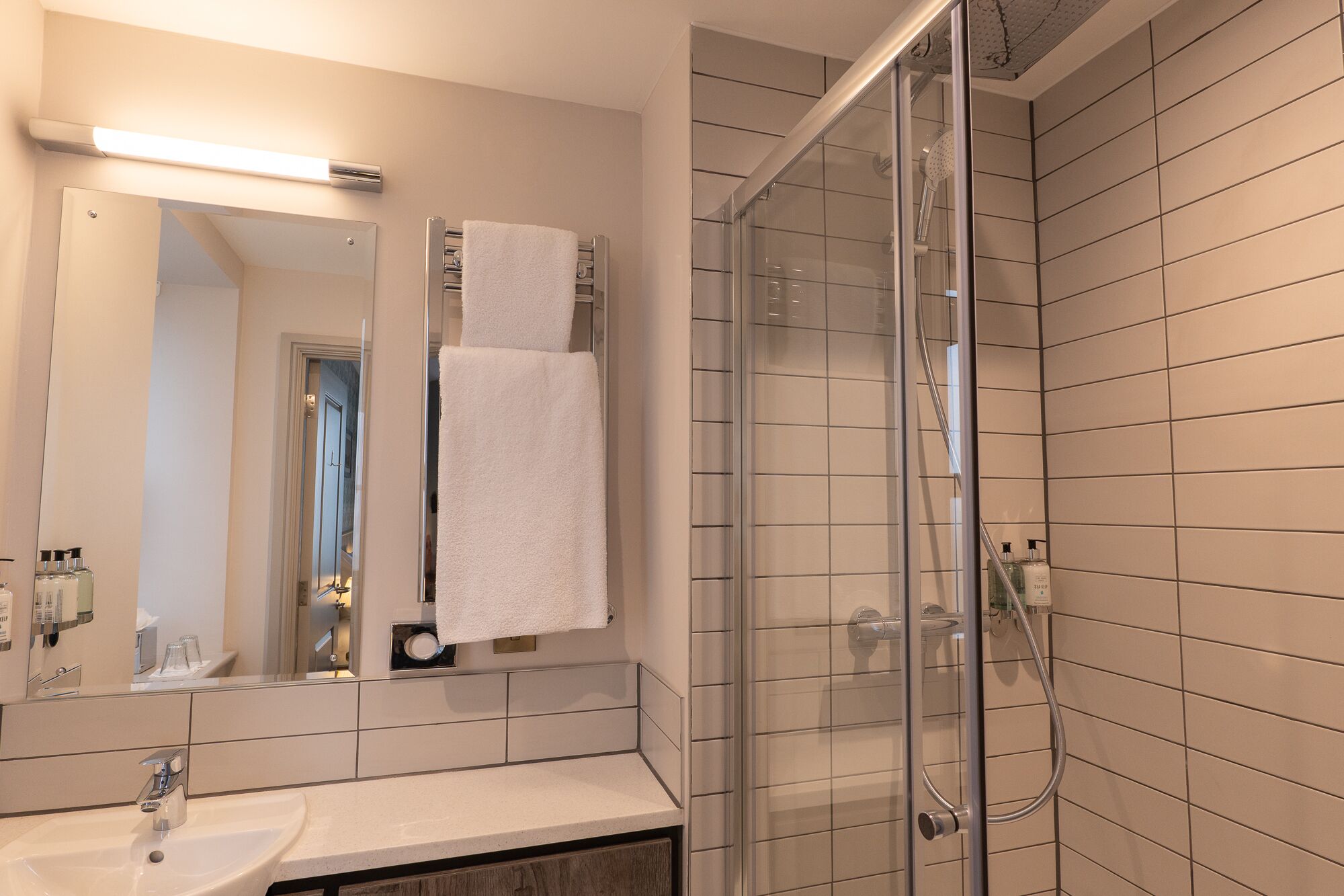 A modern bathroom with a glass shower enclosure, a sink, and a mirror.