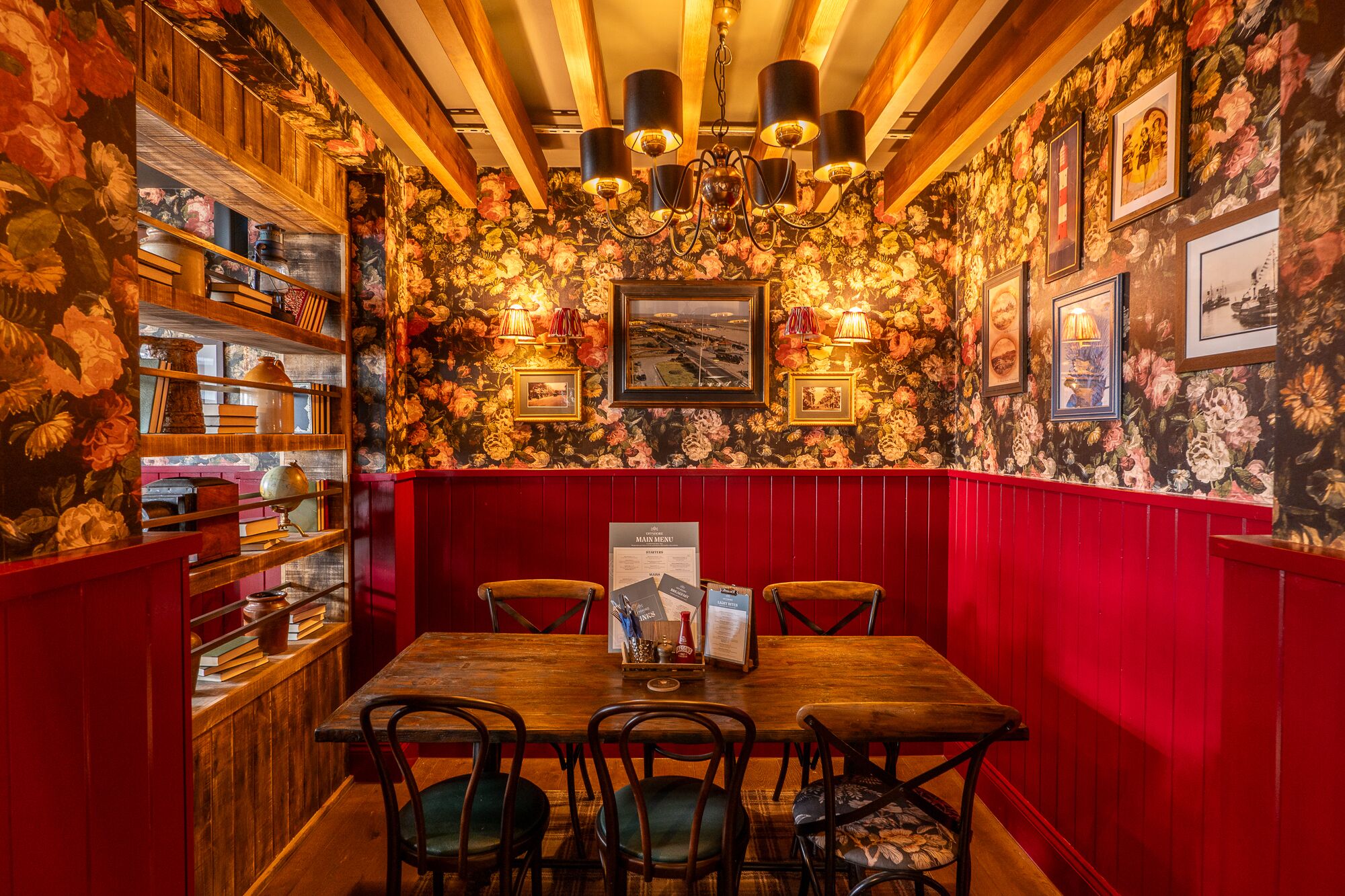 Um restaurante com interior em madeira, cabines vermelhas e papel de parede floral.