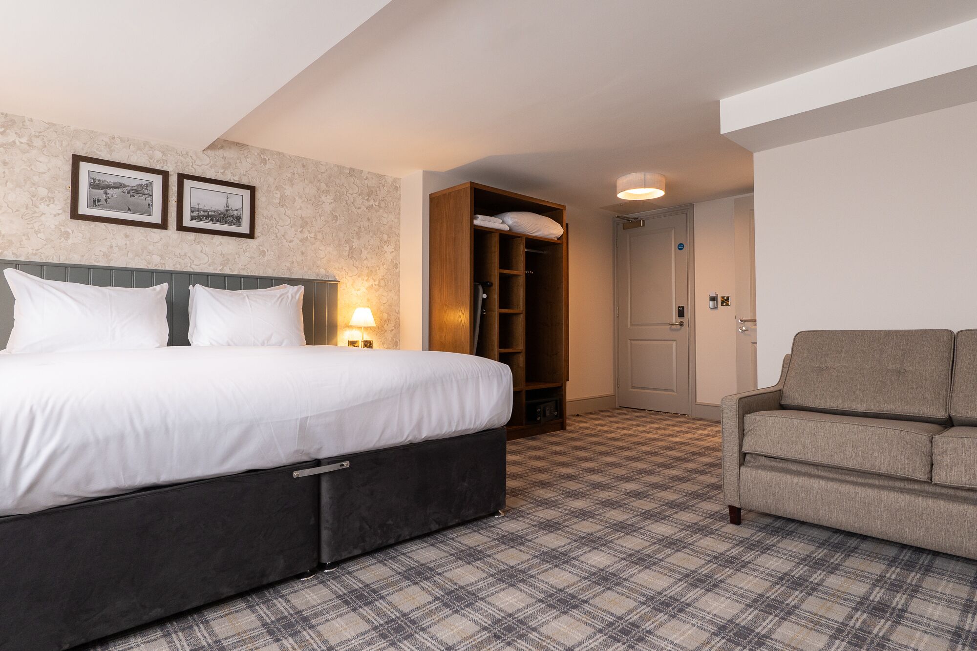 A hotel room with a bed, a wardrobe, a chair, and a check-in desk.