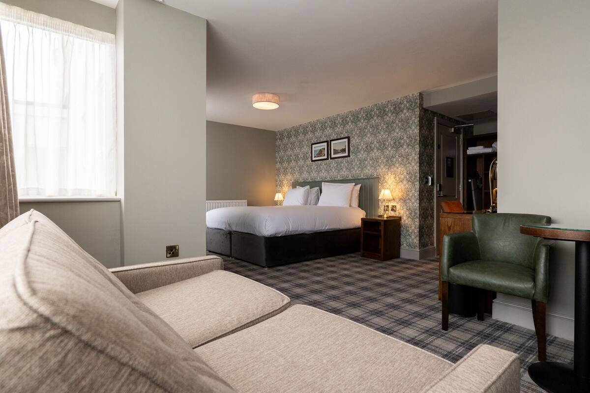 A bedroom with a bed, a green armchair, a small table, and a patterned carpet.