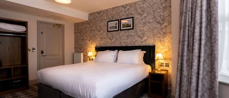 A hotel room with a large bed, two bedside lamps, a wardrobe, and a floral-patterned wall.