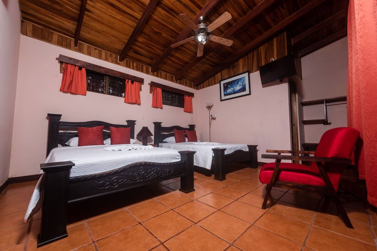 A room with two beds, a red chair, a ceiling fan, and a framed picture on the wall.