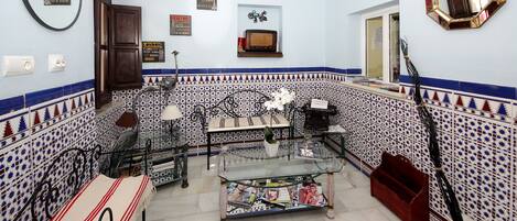 A room with a tiled wall, a glass coffee table with magazines, a bench, a mirror, and a window.