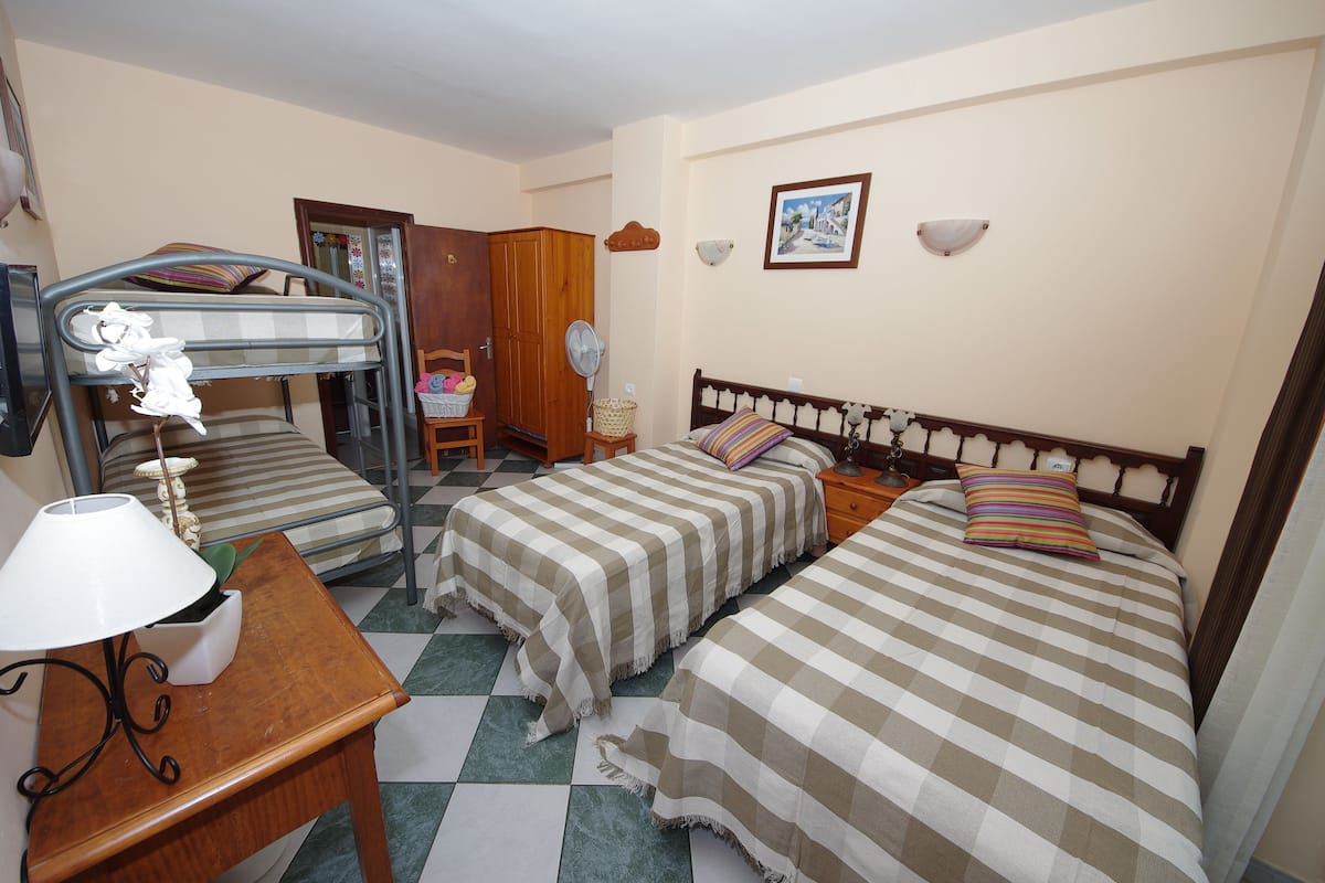 A bedroom with two single beds, a wooden nightstand, a lamp, and a small table with a plant.