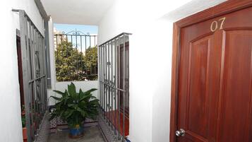 A narrow hallway with a wooden door marked "07" and a metal gate leading to a balcony with potted plants.