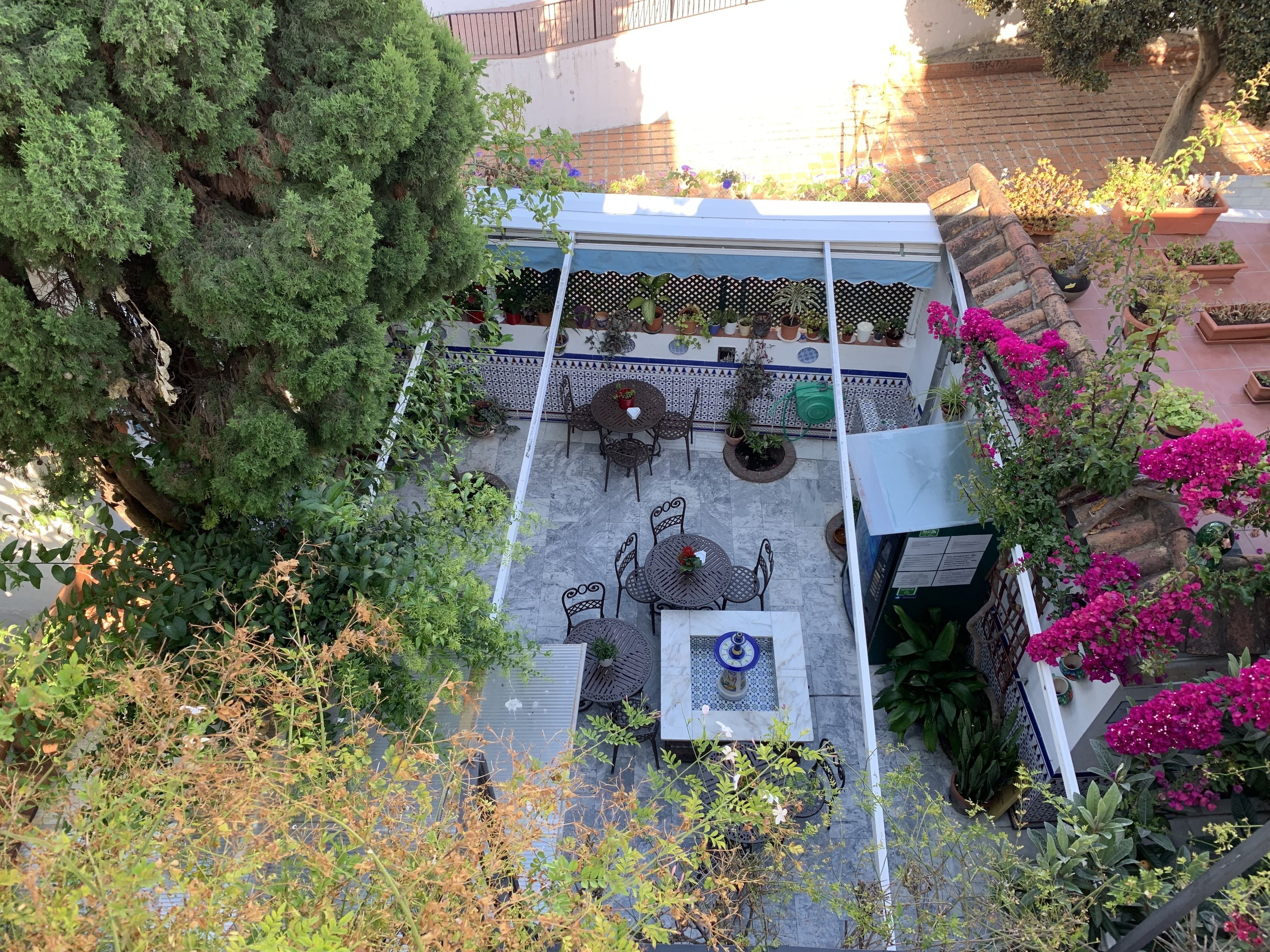 Un patio al aire libre con espacios de estar, plantas en macetas y piso de baldosas.