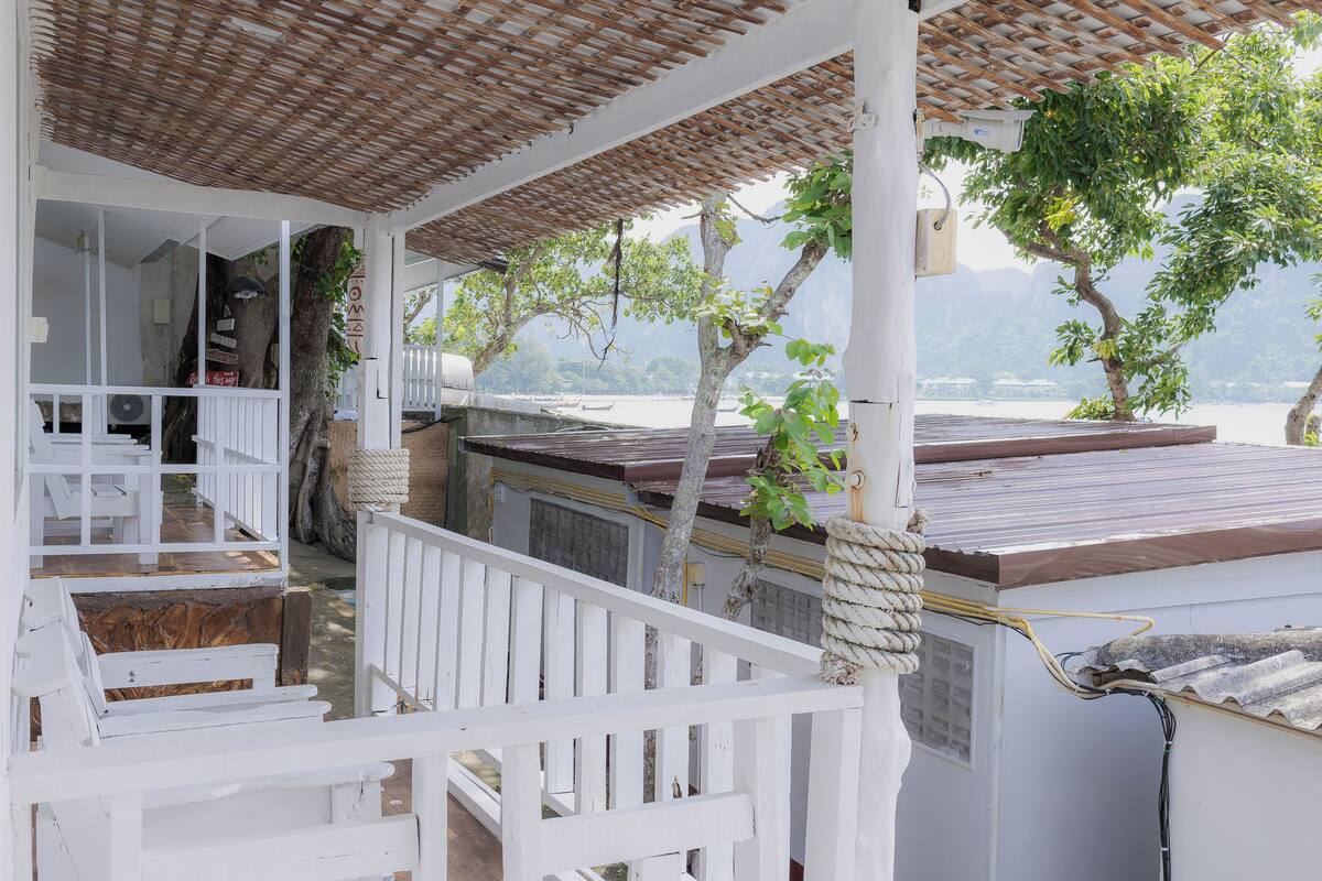 Un espacio al aire libre cubierto con un piso de madera, barandillas blancas y vista al mar.