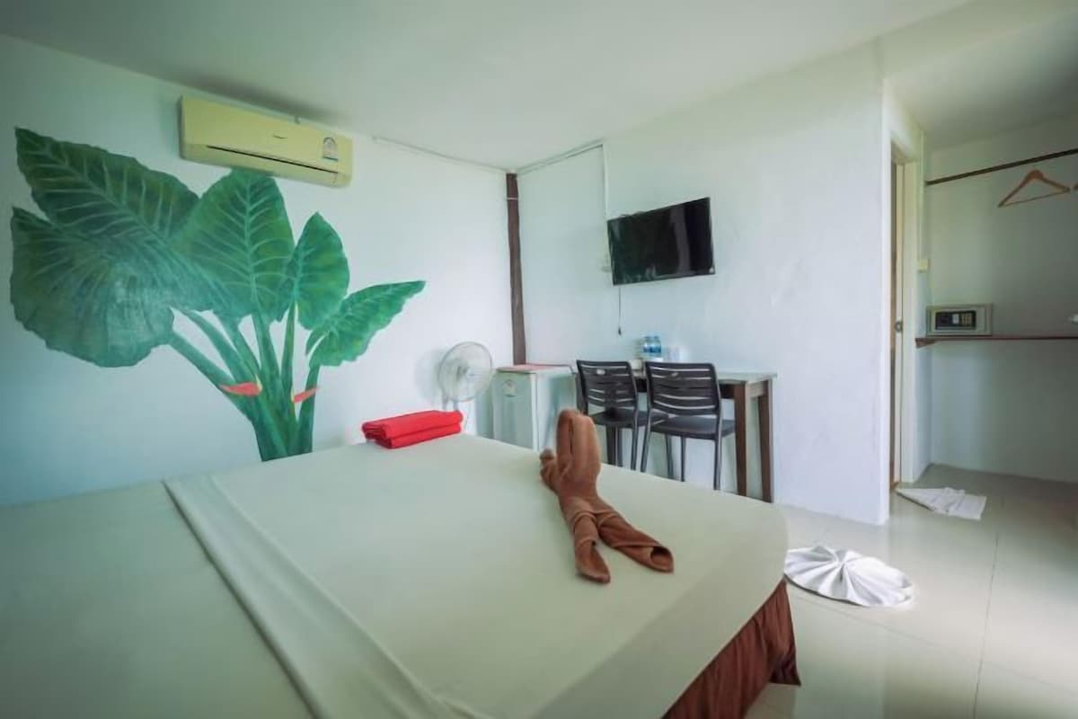 A hotel room with a bed, a desk with a chair, a TV, and a wall-mounted air conditioner.
