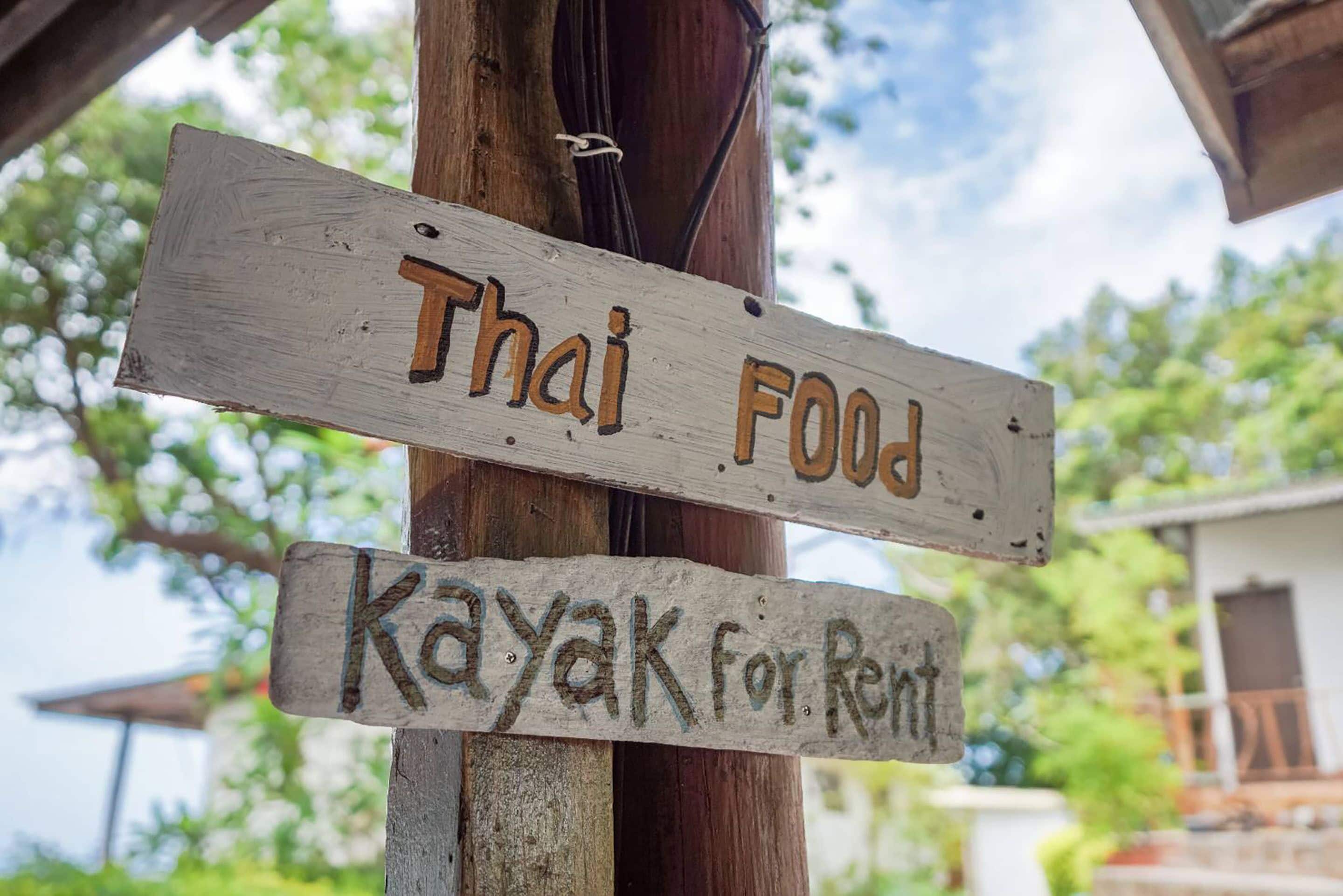 Un letrero de madera que dice 'Thai Food' y 'Kayak para Alquilar'.