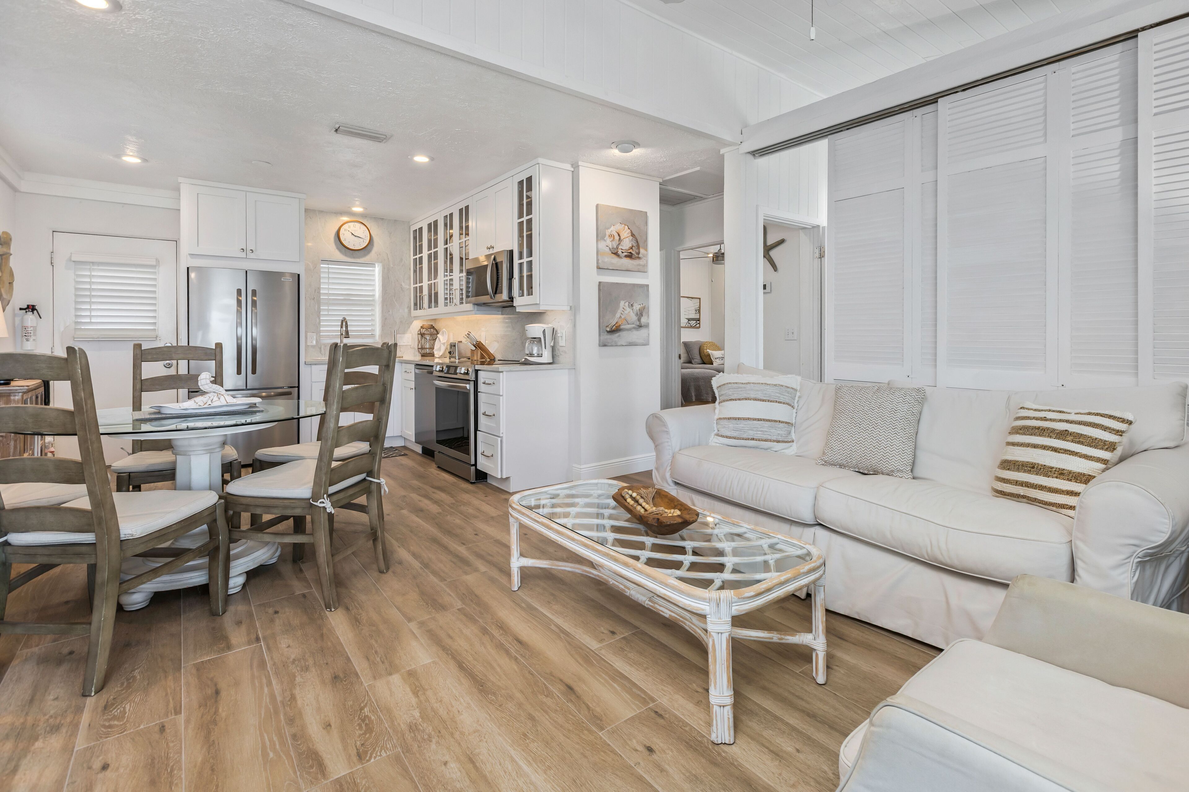 A modern kitchen with white cabinetry, a dining area with wooden chairs, and a white sofa with striped pillows.