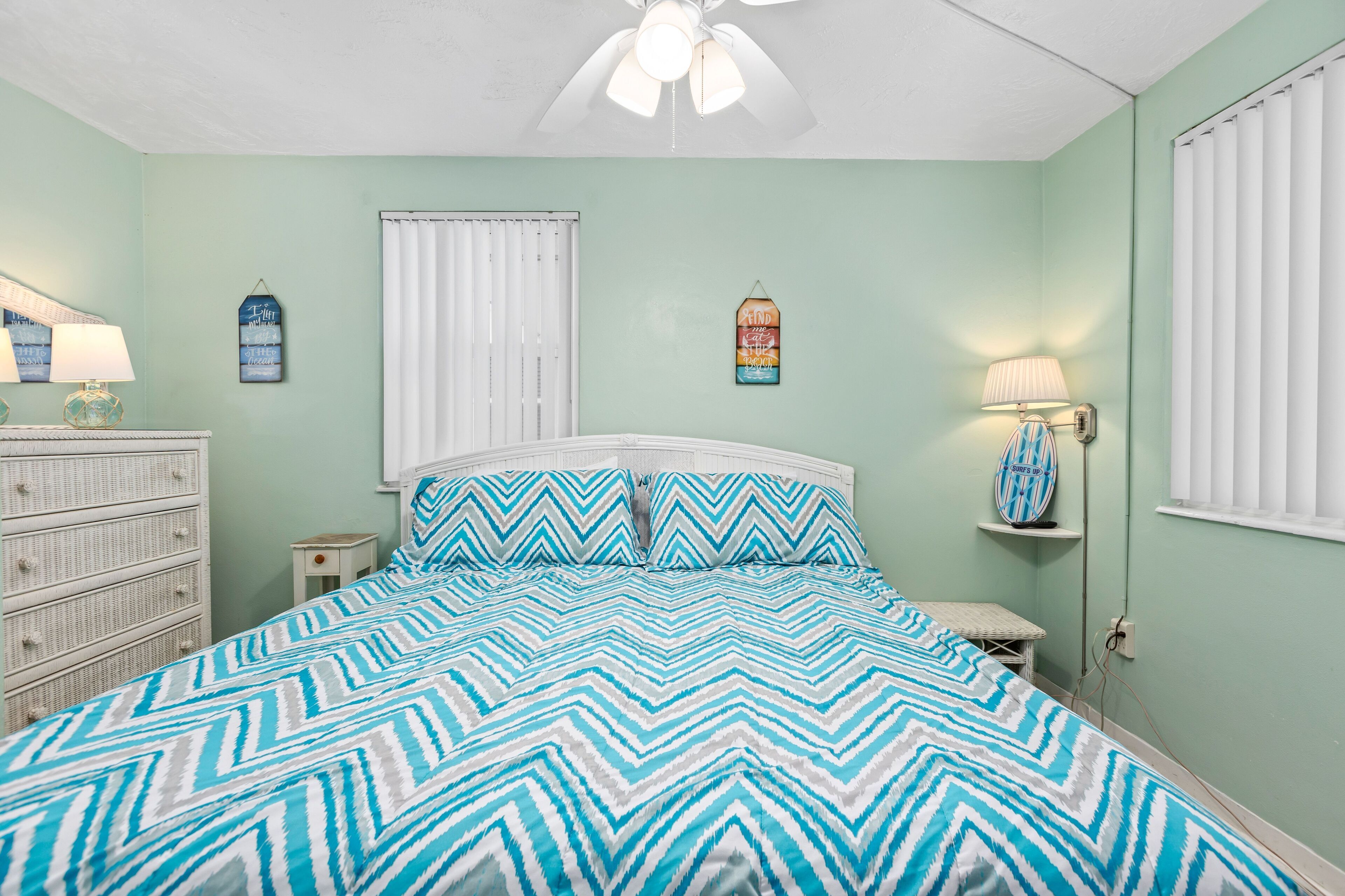 Ein Schlafzimmer mit Bett, Schminktisch, Nachttisch und Deckenventilator.