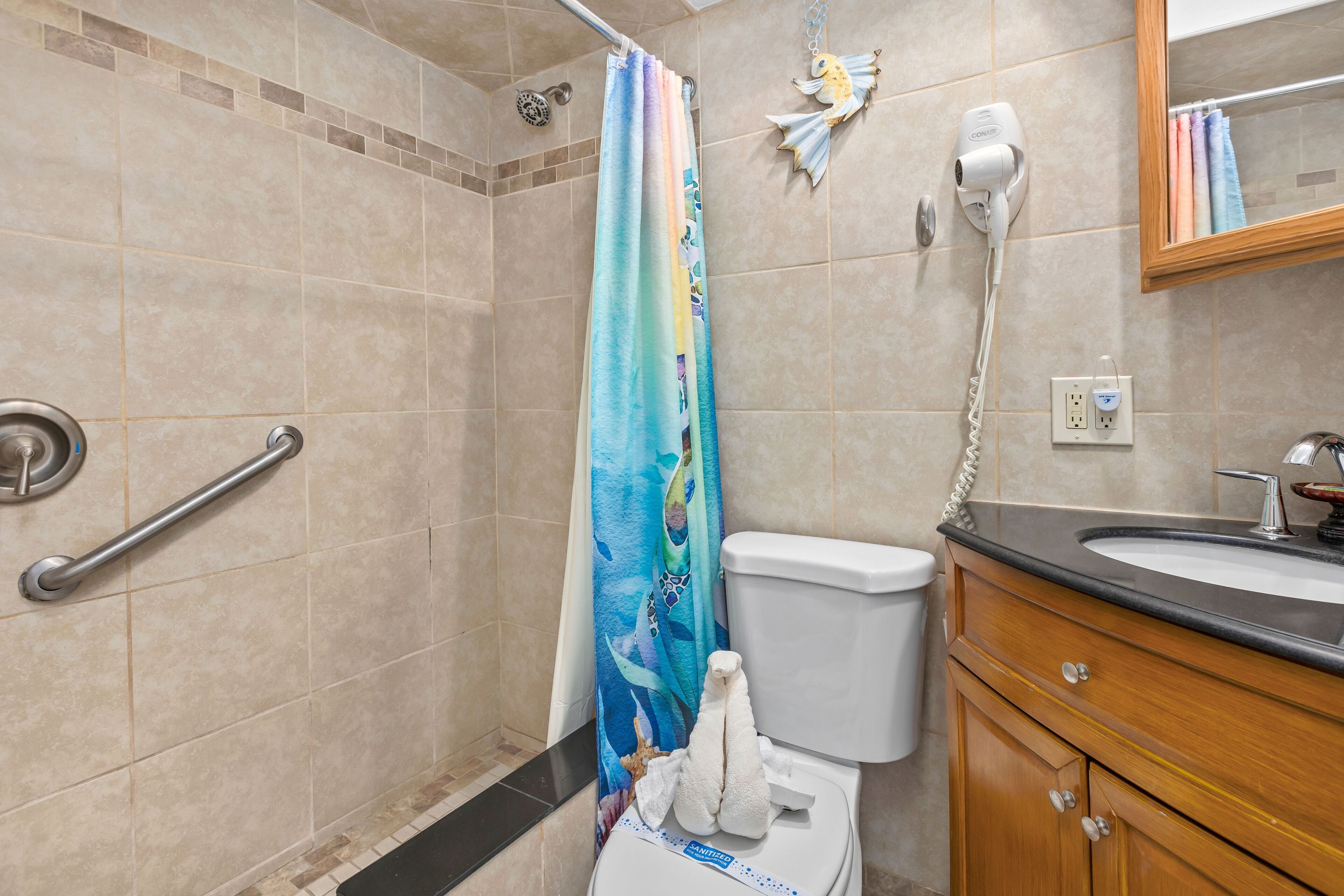 A bathroom with a shower, toilet, vanity, and a hand dryer.