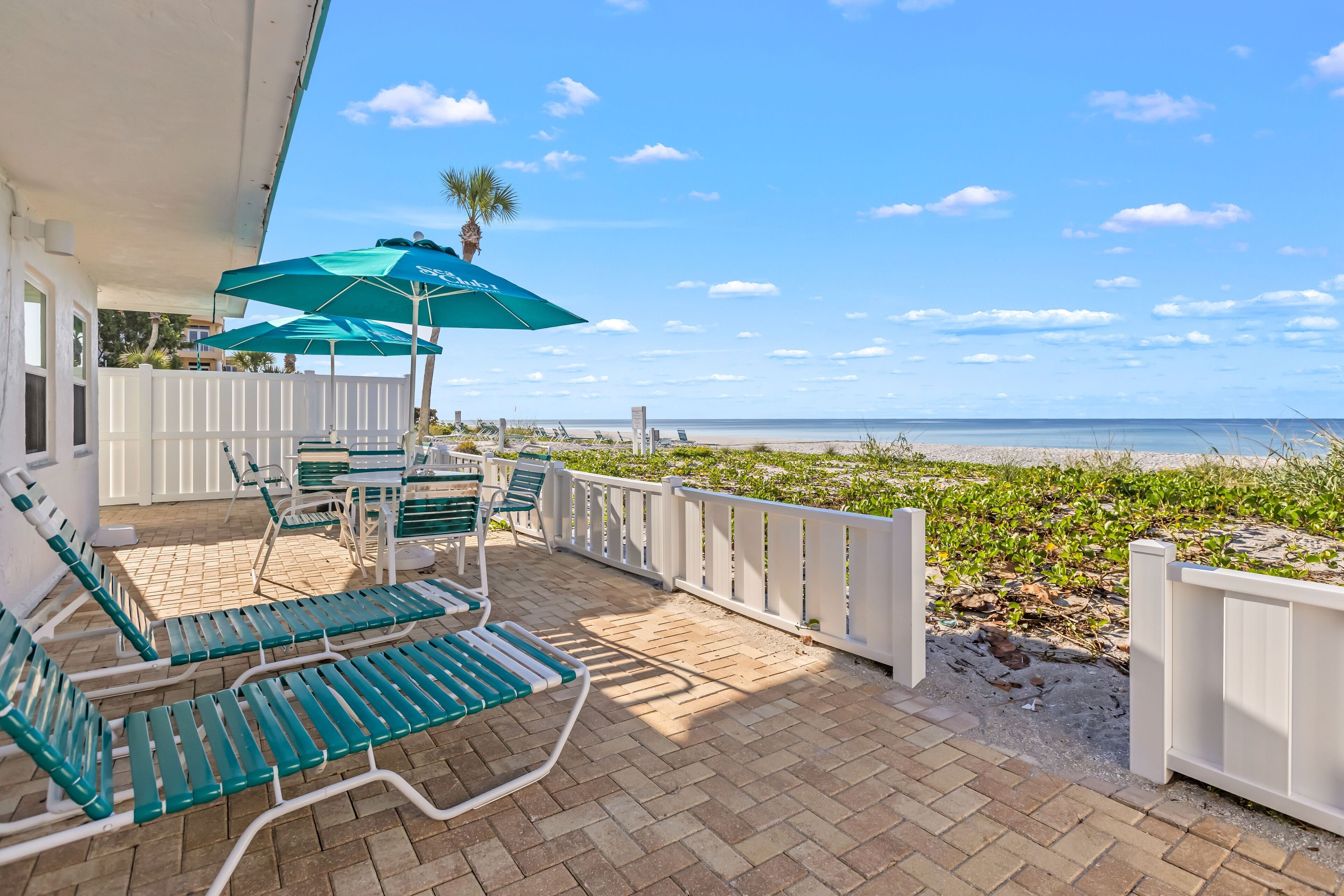 Une terrasse couverte, dotée de fauteuils de jardin verts et de parasols, qui offre une vue sur la plage.