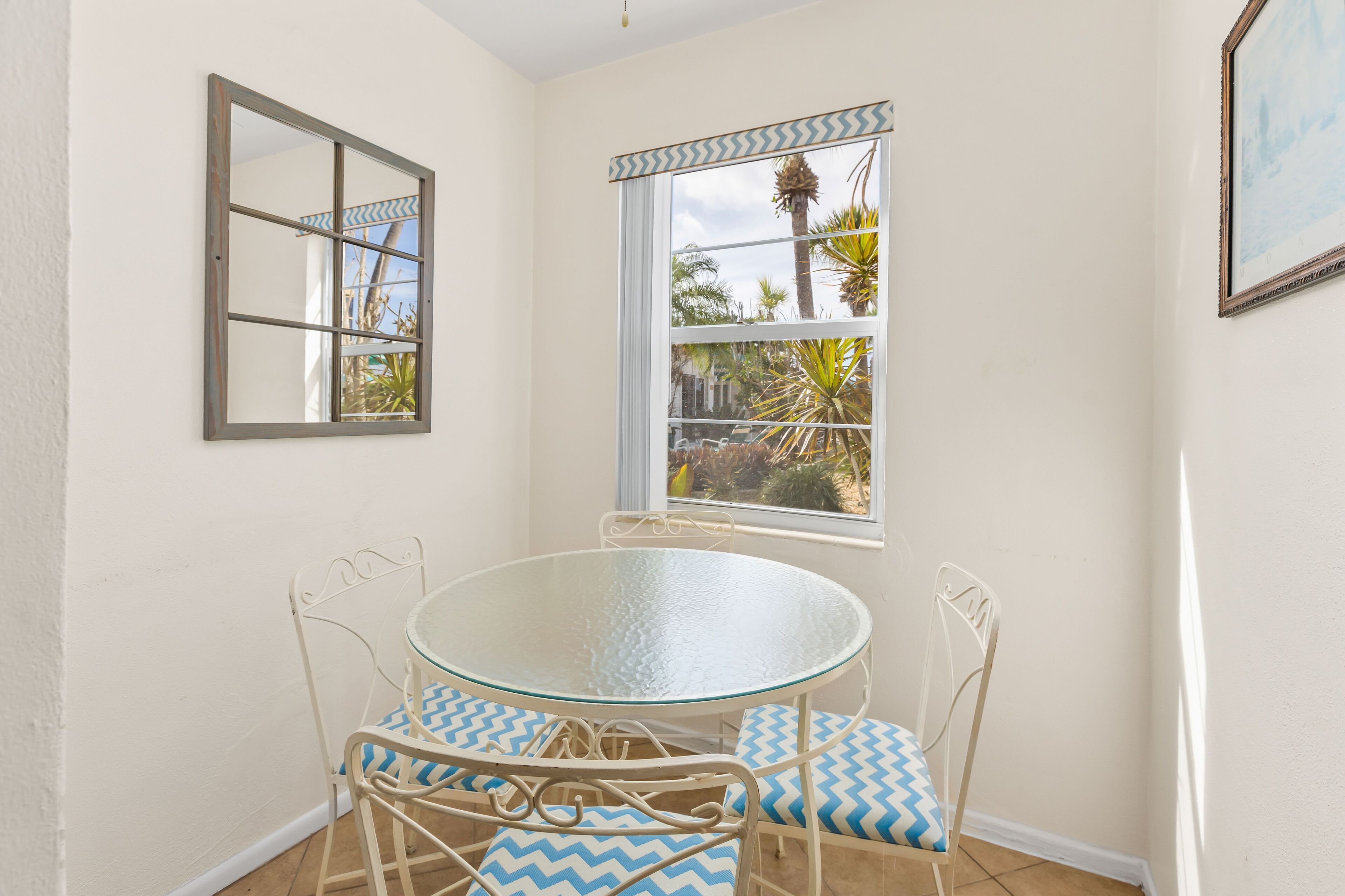 Un comedor con una mesa redonda de vidrio y sillas de metal blanco con cojines estampados en azul y blanco.