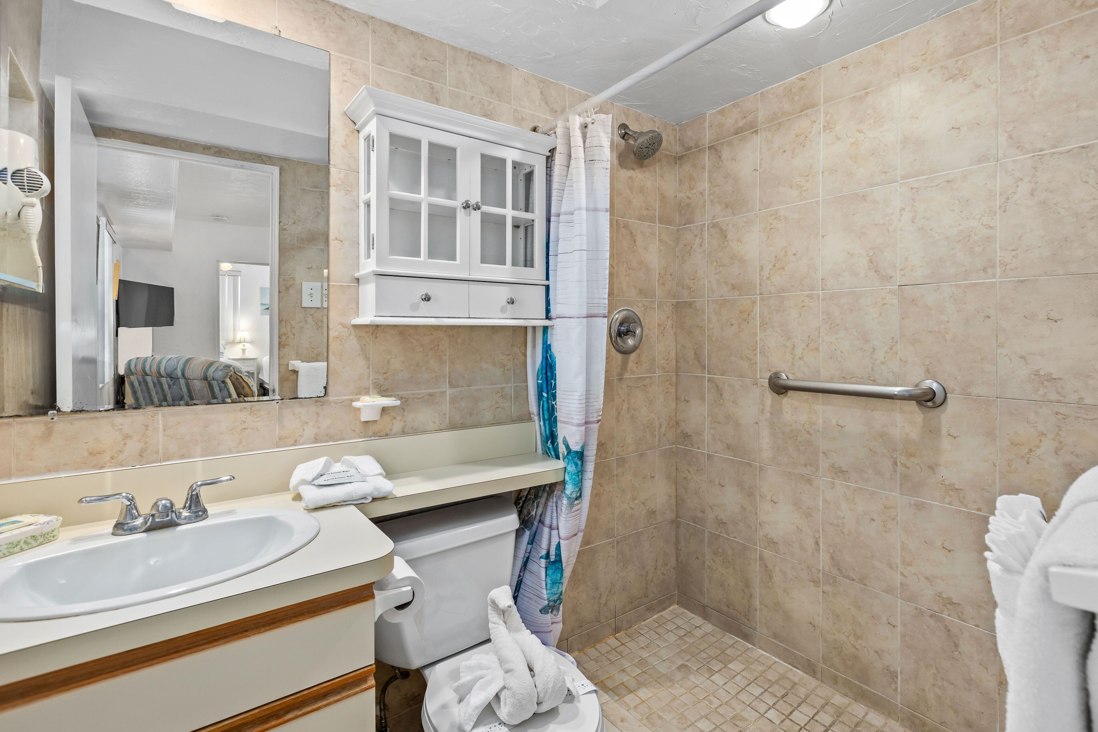 A bathroom with a sink, mirror, cabinet, shower, and a handrail.