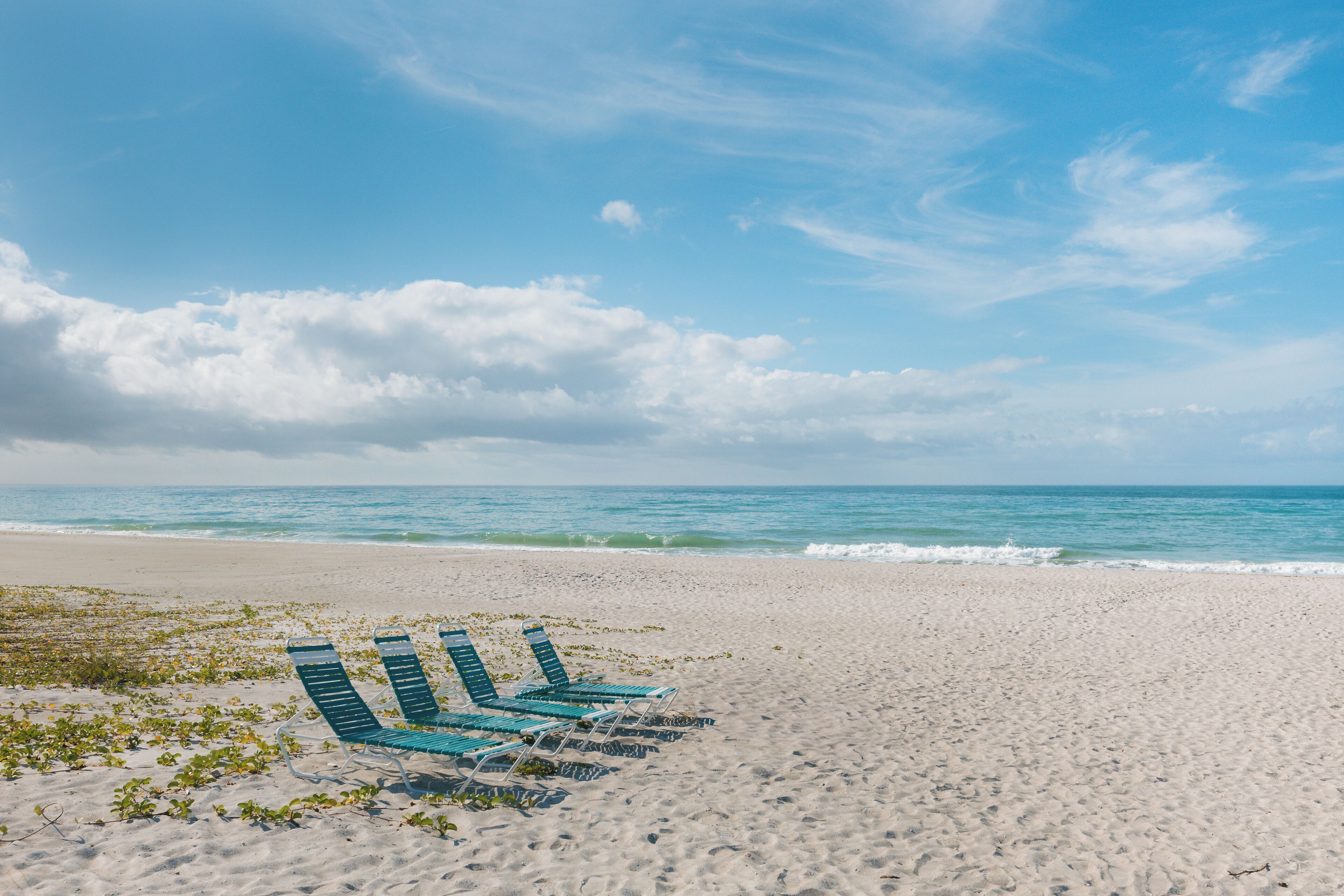 Ein Strand mit einer Reihe leerer blauer Liegestühle, die zum Meer blicken.