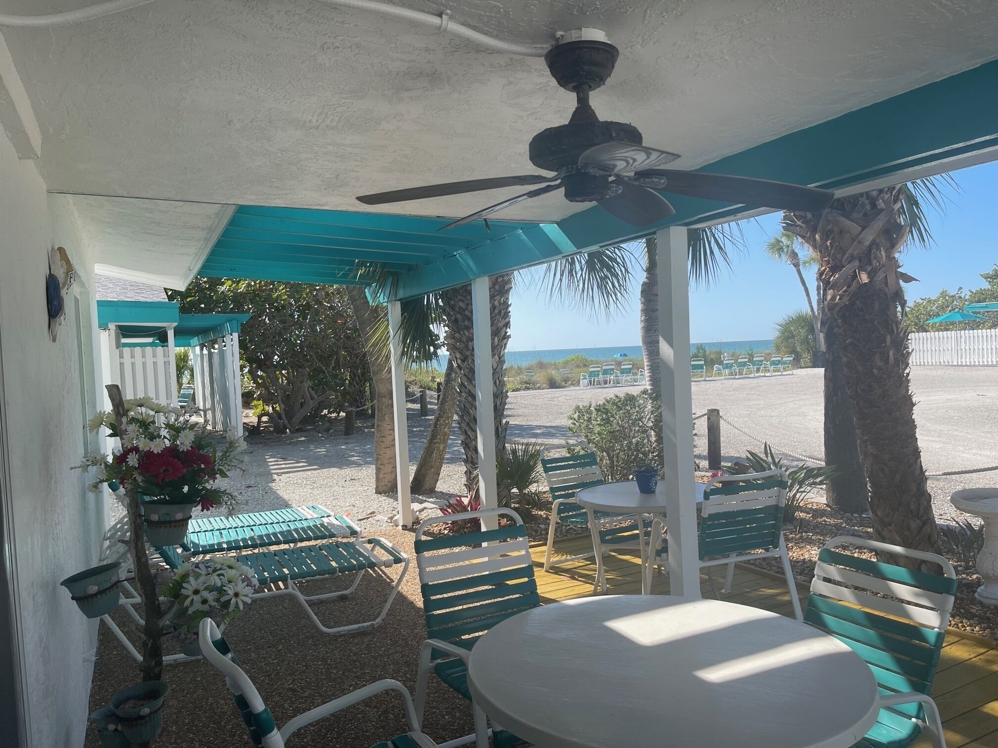 A covered outdoor seating area with tables and chairs, a ceiling fan, and a view of the beach.