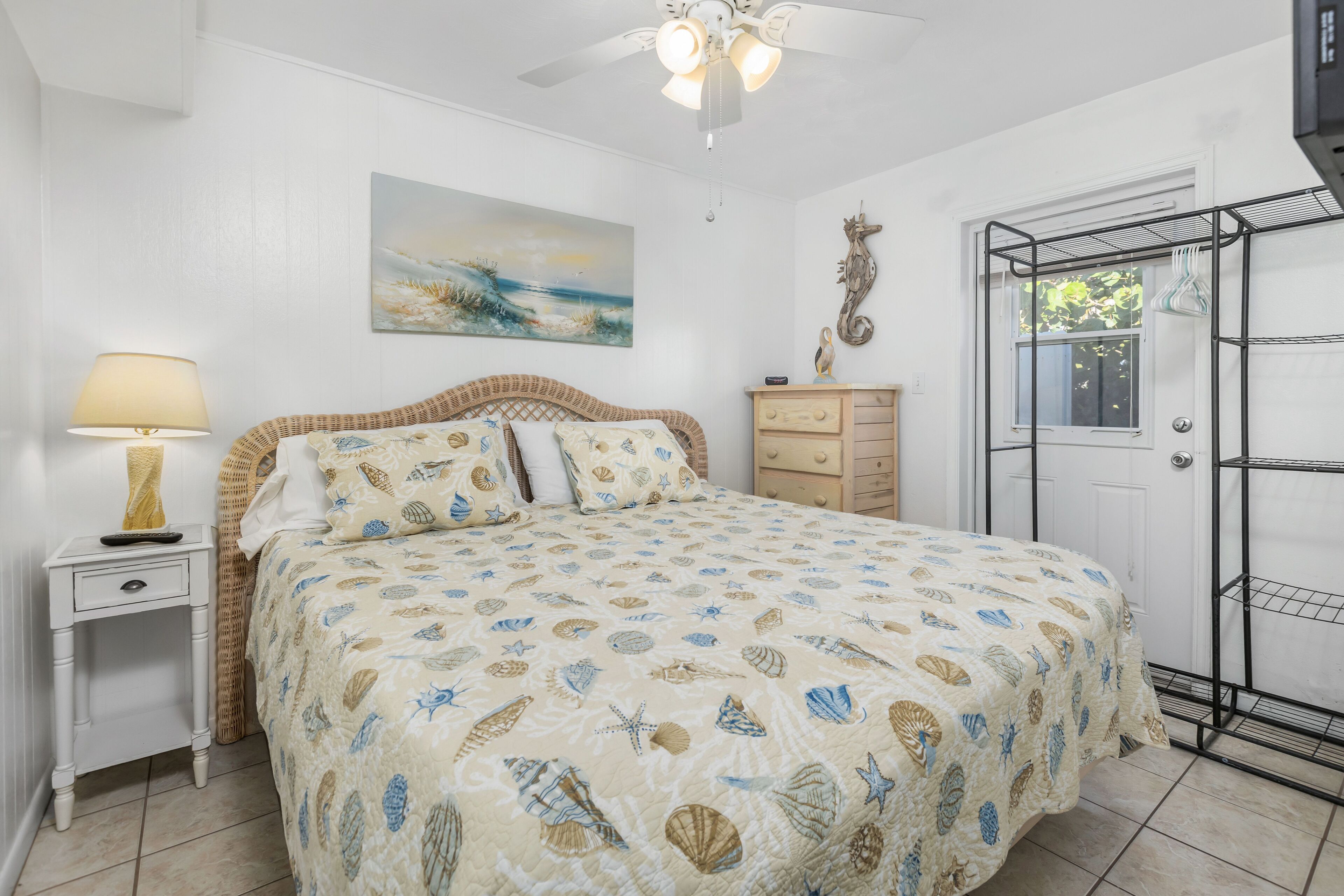 A bedroom with a bed, a nightstand, a lamp, a dresser, a door, and a ceiling fan.