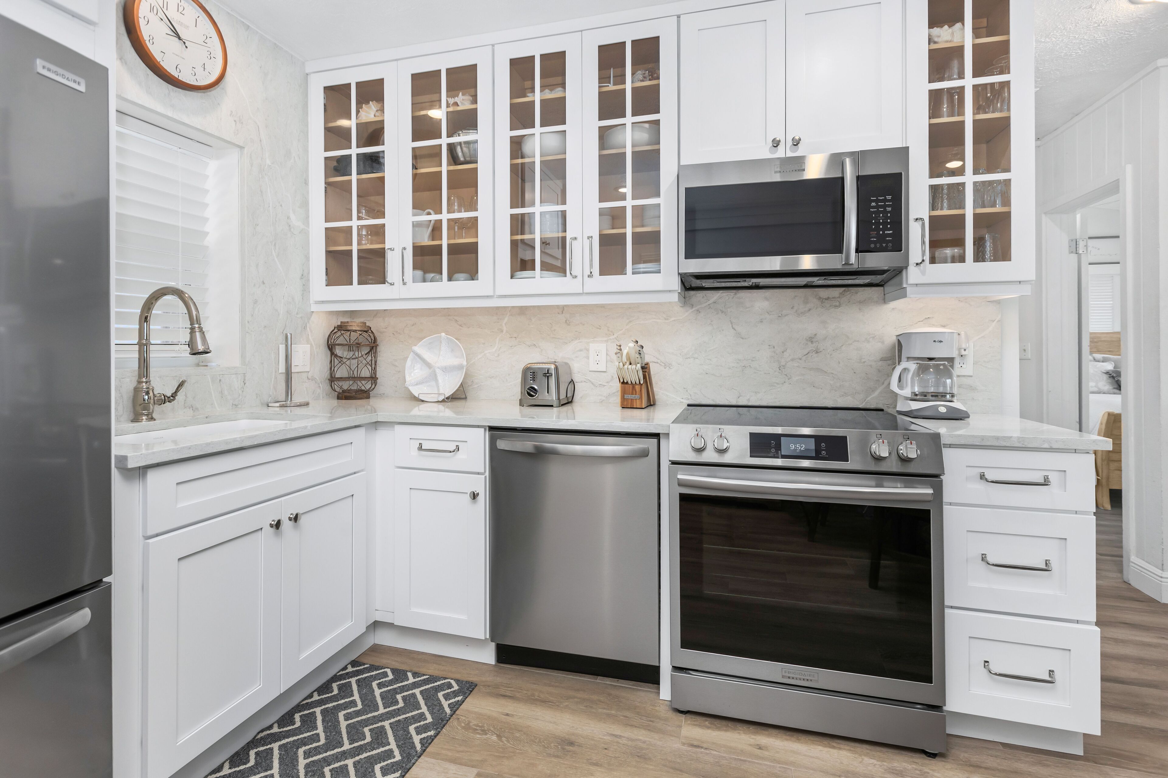 A modern kitchen with white cabinetry, a stainless steel refrigerator, a microwave, a dishwasher, and an oven.