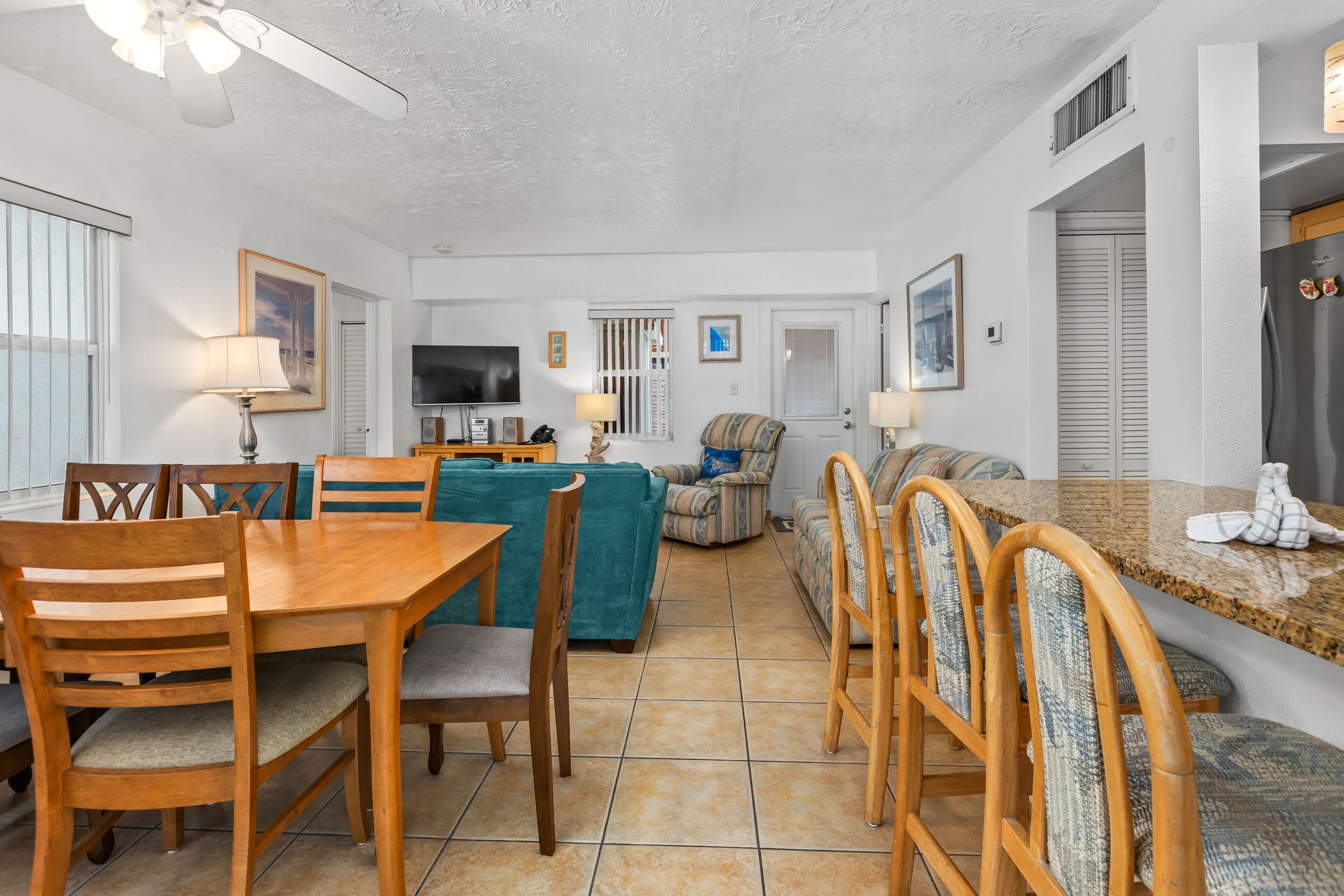 A spacious living area with a dining table, chairs, a sofa, and a kitchen area with a refrigerator and microwave.