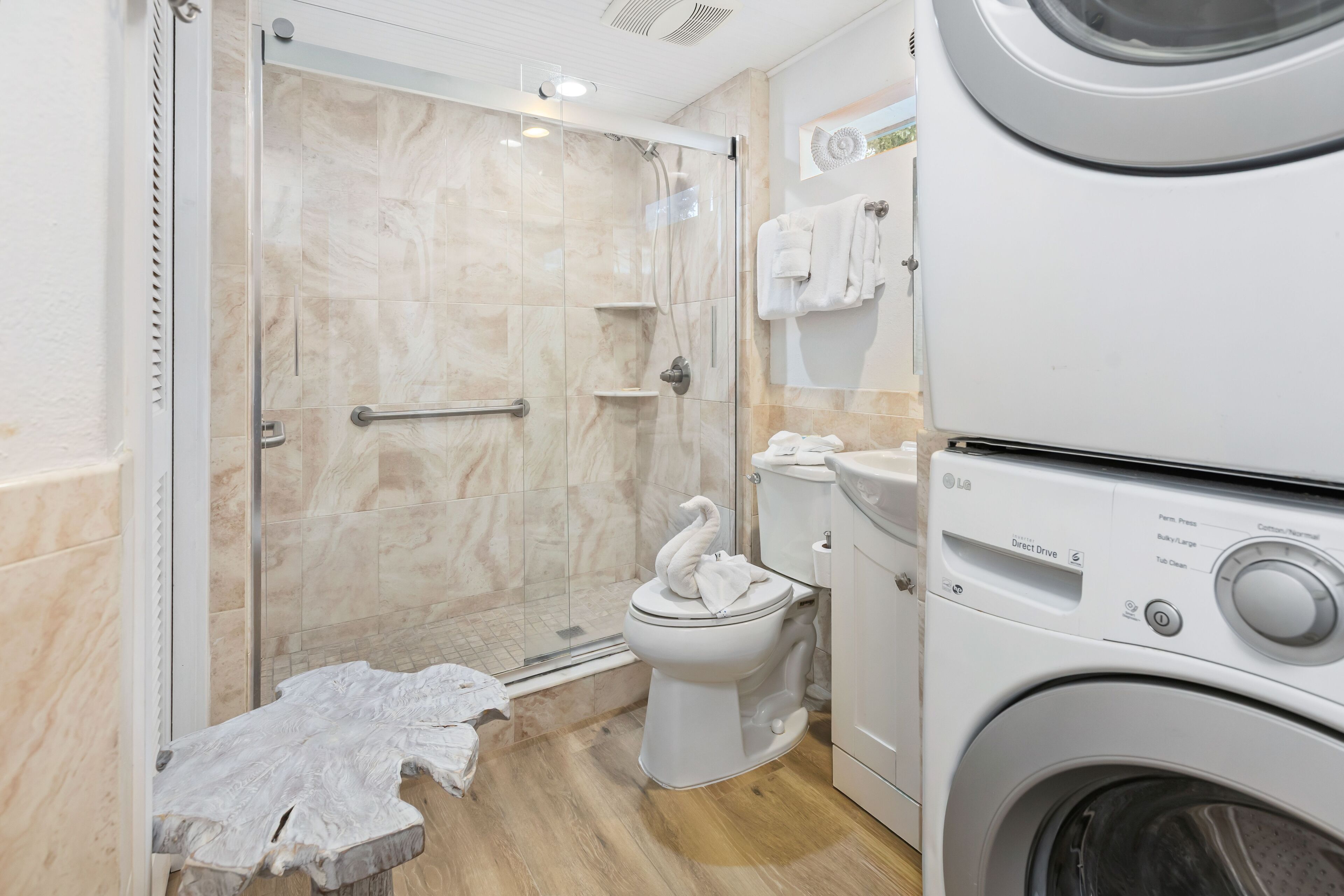 Une salle de bain avec une douche à parois de verre, des toilettes et un lave-linge et un sèche-linge superposés.