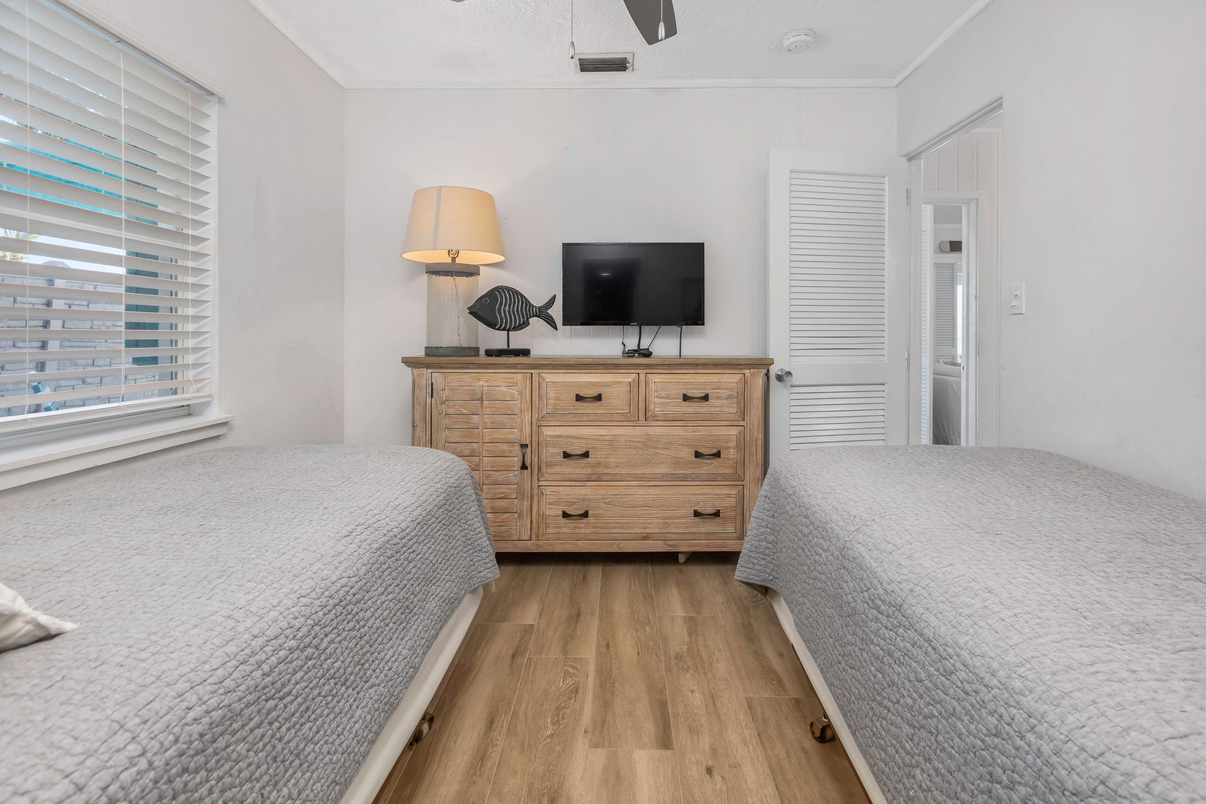 A bedroom with two beds, a TV, a dresser, and a window with blinds.