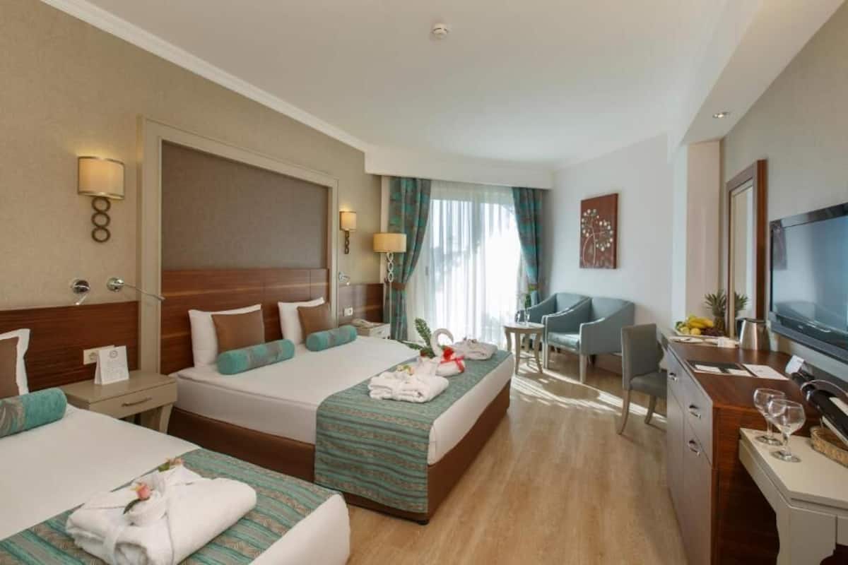 A hotel room with two beds, a desk with a TV, and a seating area with a chair and table.