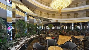 Un vestíbulo de hotel de varios niveles con un atrio central, que incluye zonas de estar escalonadas, una gran araña y un elemento decorativo de agua.