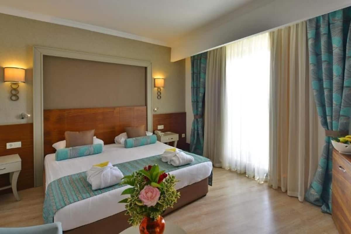 A hotel room with a large bed, bedside tables, a desk, a TV, and curtains.
