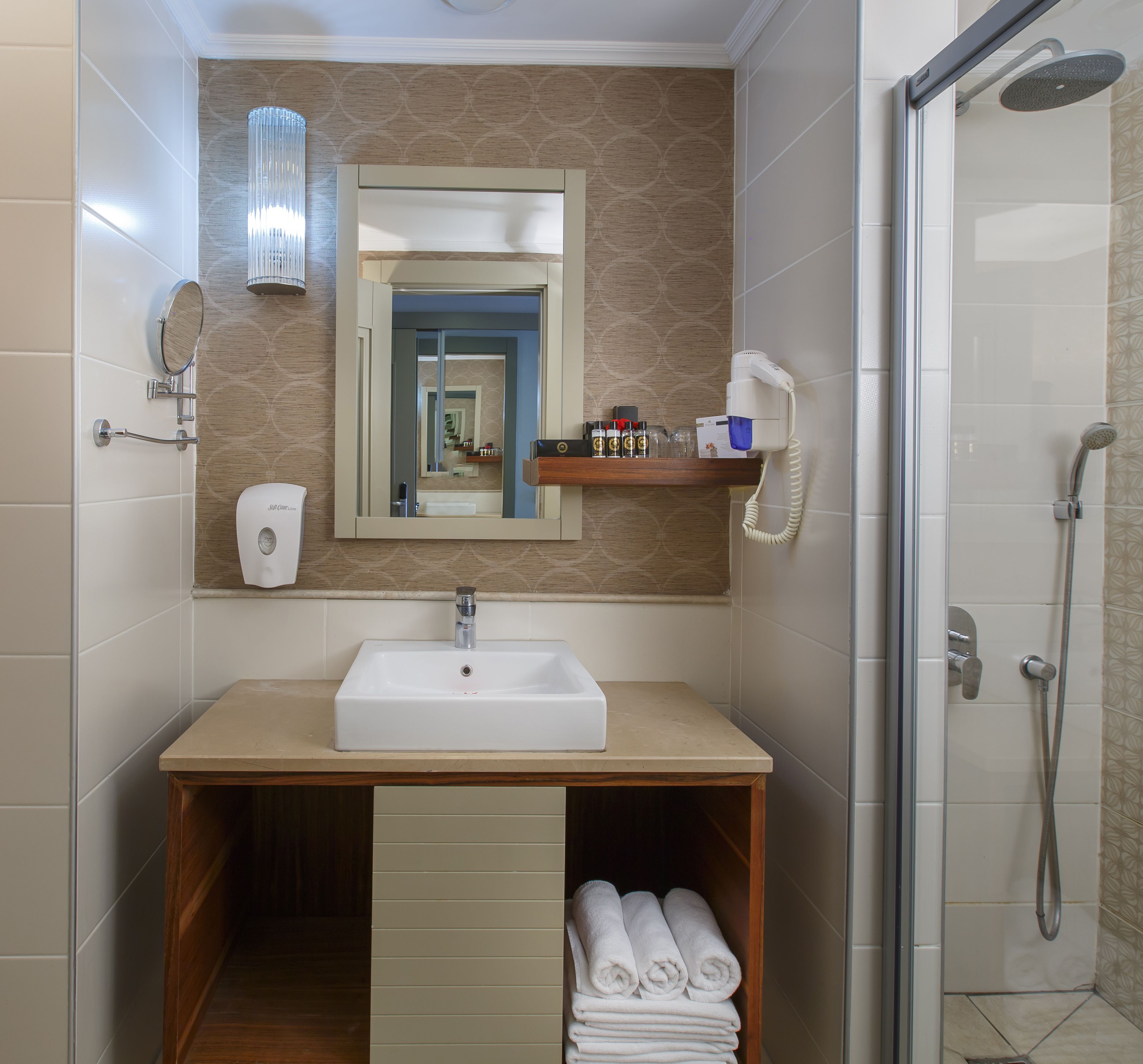 Un baño con lavamanos, espejo, toallero y ducha.