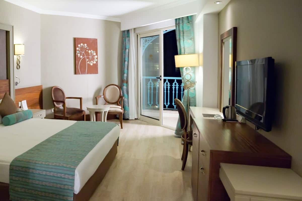 A hotel room with a bed, a desk, a chair, a TV, and a balcony with curtains.