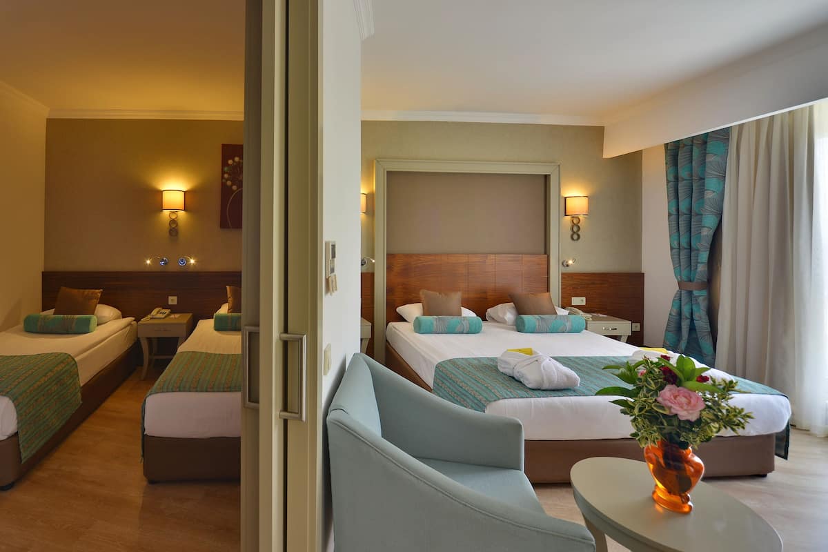 A hotel room with two single beds, a double bed, a sofa, and a small table with a vase of flowers.