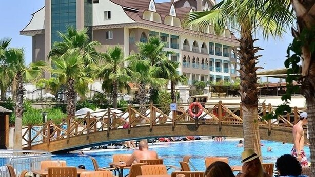 Un resort con zona de piscina, palmeras y un edificio grande de estilo arquitectónico distintivo.