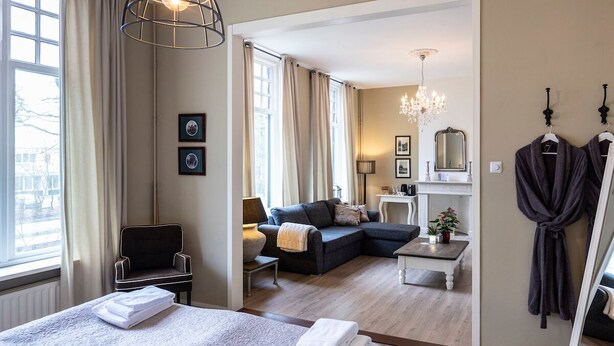 A hotel room with a large bed, a sofa, a chair, a small table, and a robe hanging on the wall. - Bed & Breakfast Rijsterbosch (Rijs)