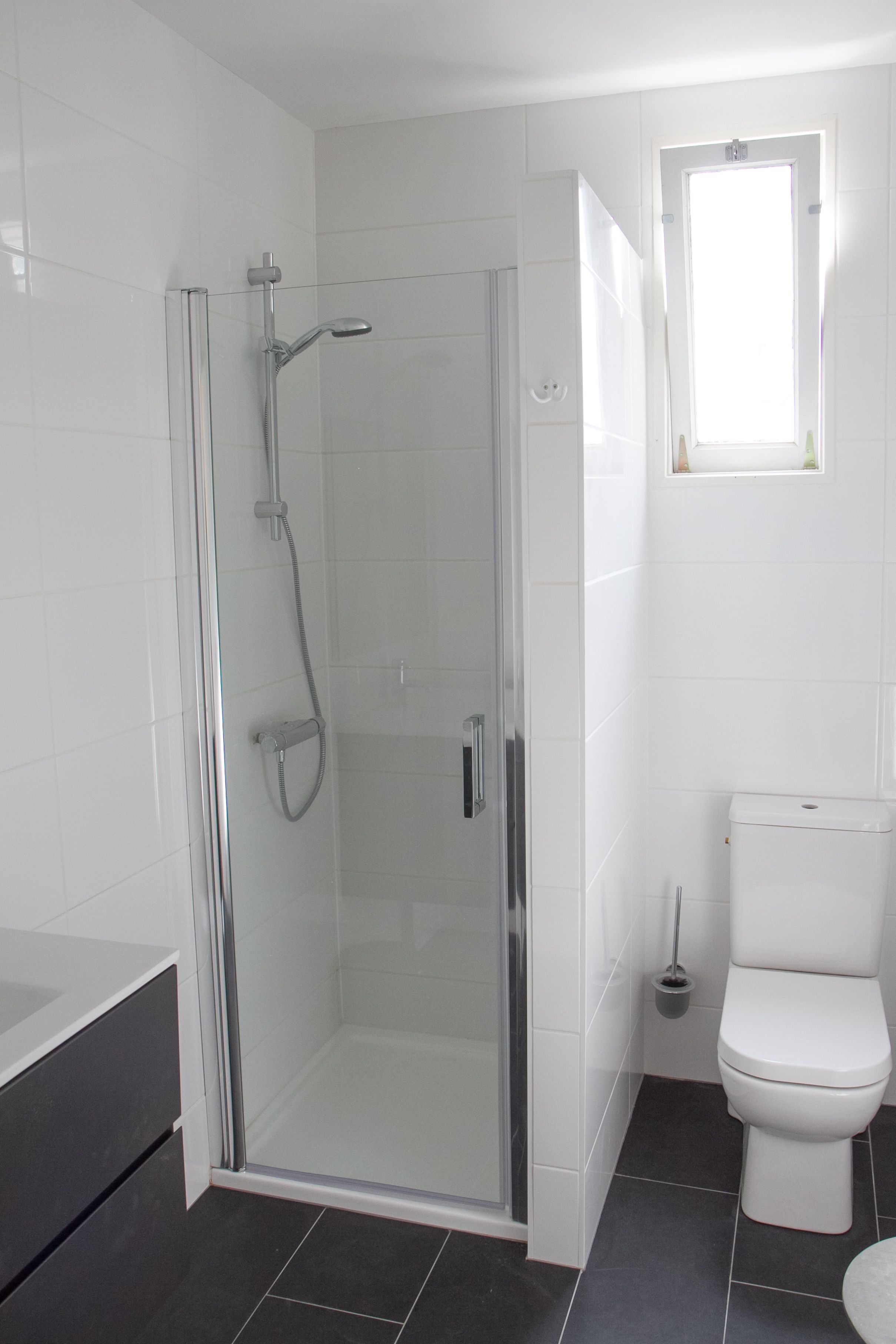 A modern bathroom with a glass-enclosed shower, a white toilet, and a small window.